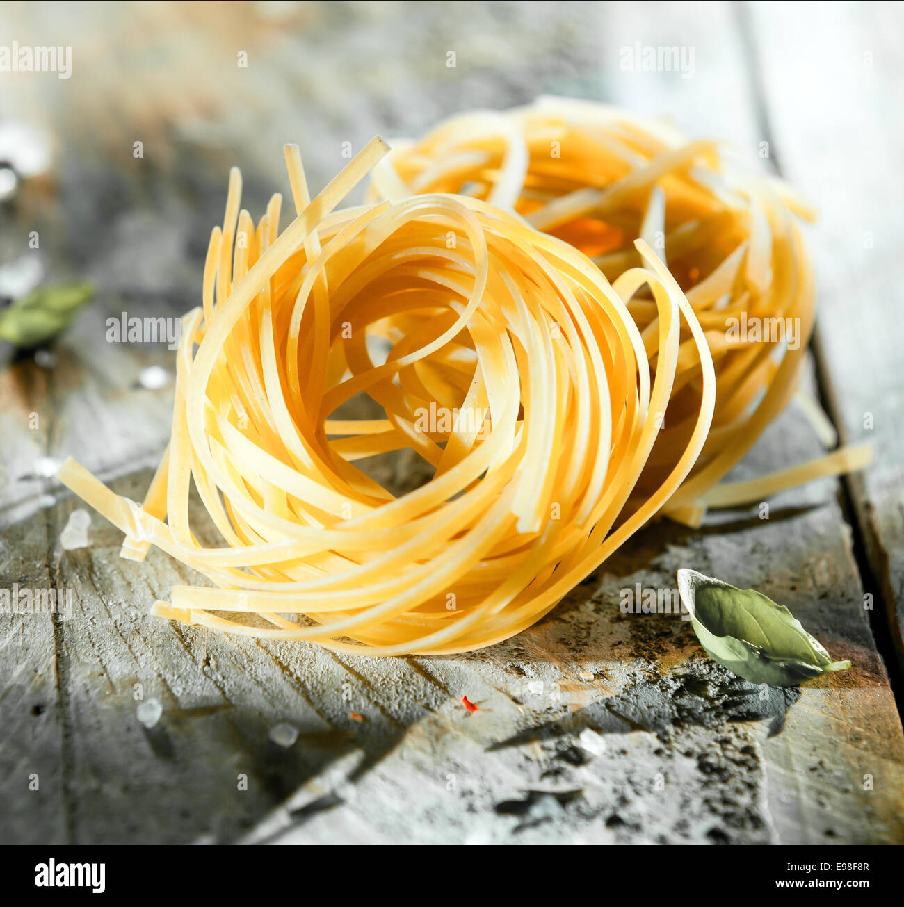 Uncooked coils of Italian linguine or tagliatelli pasta made from dried durum wheat dough on a grungy wooden table, square format Stock Photo