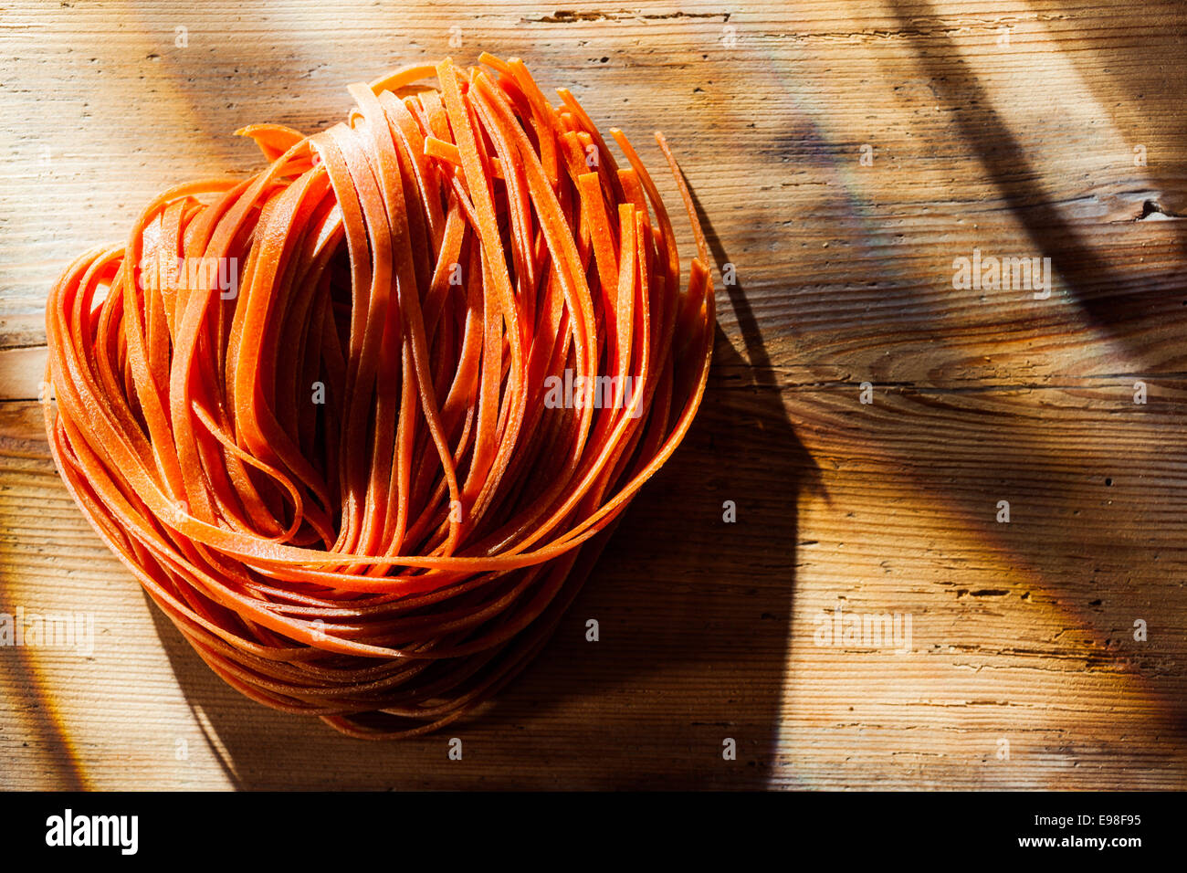 Tomato flavoured Italian tagliatelli or linguine pasta standing ready to be added to a savory pasta dish on an old wooden kitchen counter in dappled sunlight Stock Photo