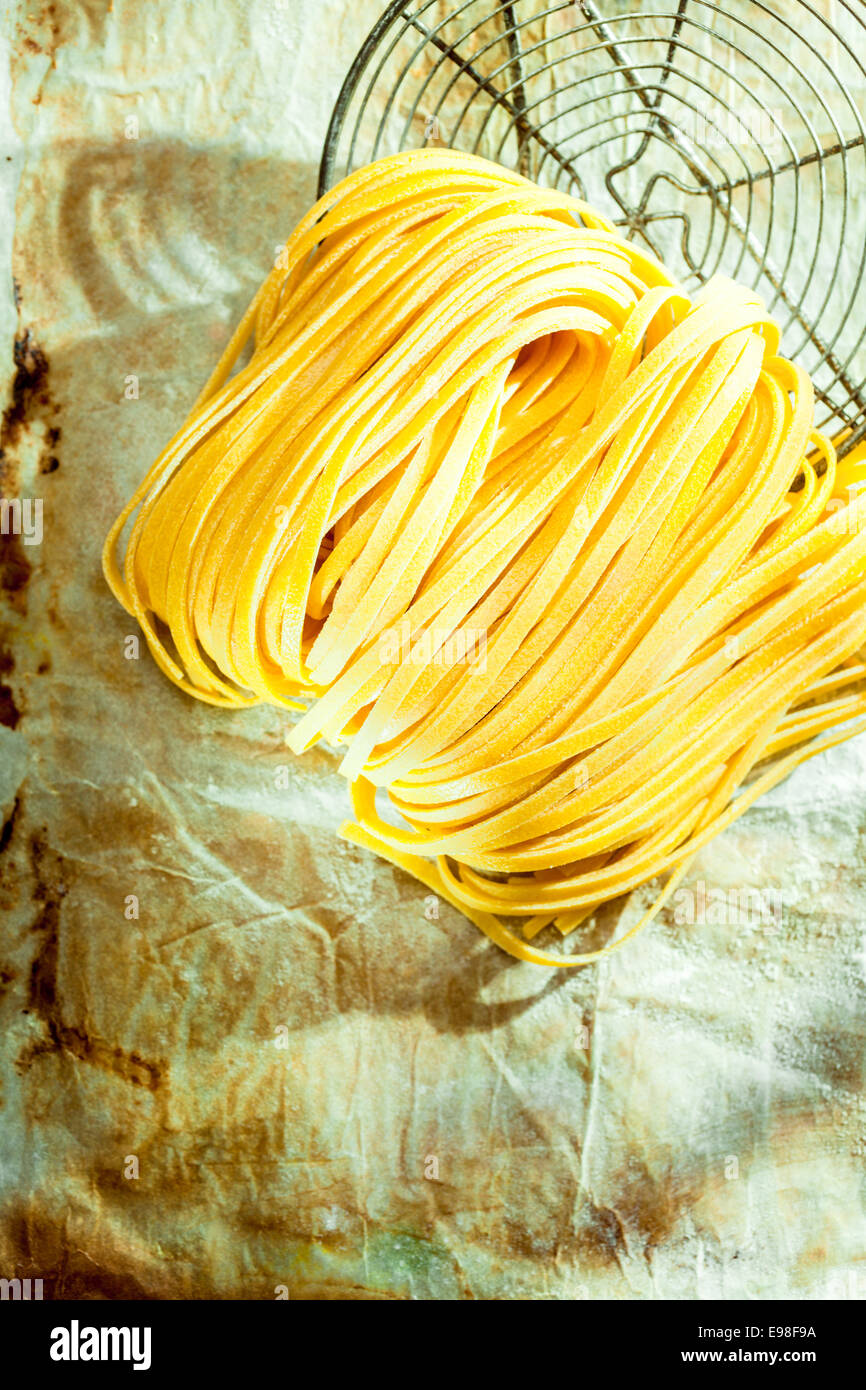 Overhead view of colied dried Italian linguine or tagliatelli egg noodle pasta lying with an old wire strainer on grunge paper with copyspace Stock Photo