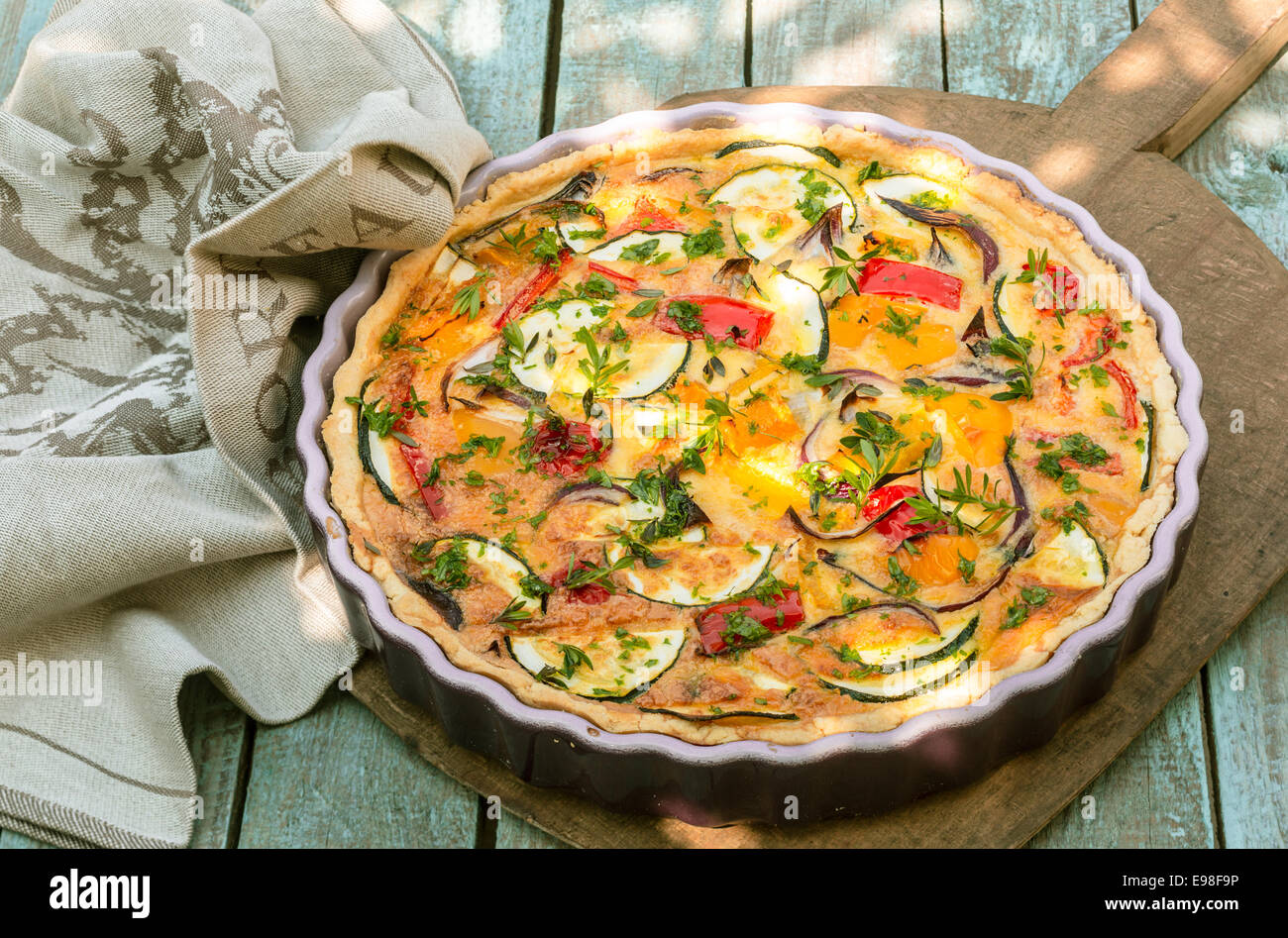Delicious eggplant savory tart with tomato and fresh herbs in a fluted pie dish served on a wooden board outdoors for a summer picnic Stock Photo