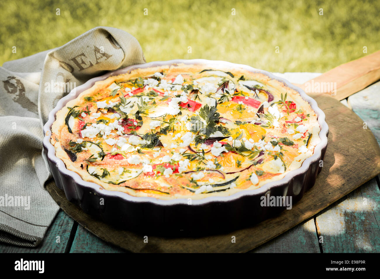 Tasty vegetarian quiche on a summer picnic table outdoors with eggplant, eggs, cheese, tomato and herbs for a healthy lunchtime Stock Photo