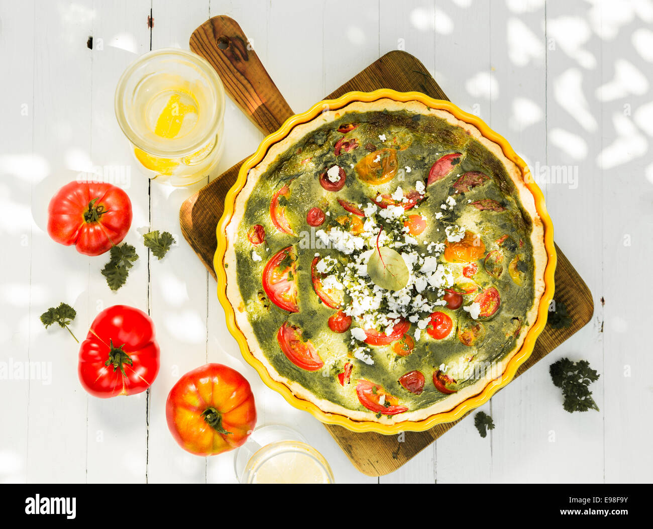 Savory quiche with egg, tomatoes, cheese and herbs viewed from above on a wooden chopping board with fresh tomatoes on a rustic Stock Photo