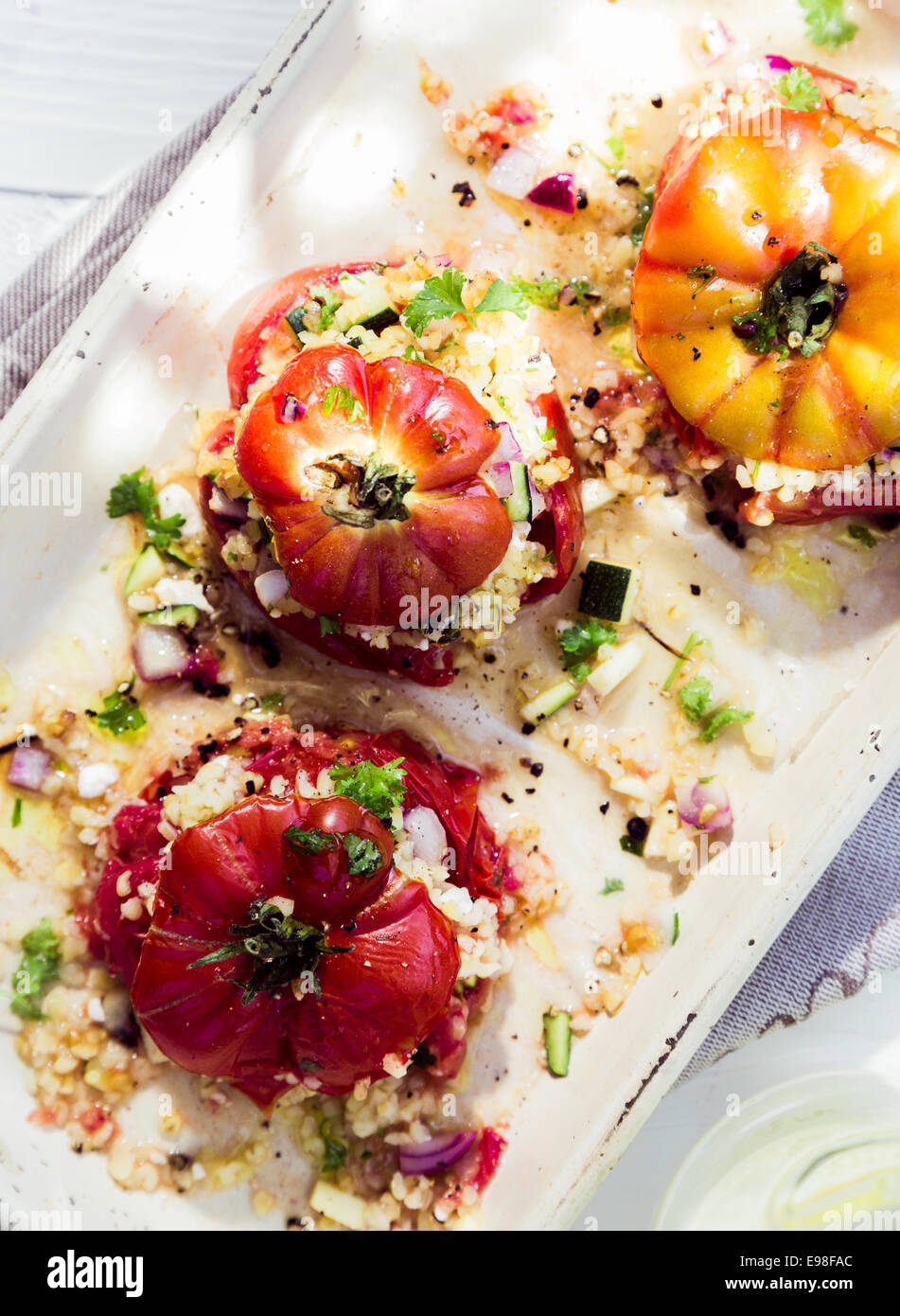 Cooked baked tomatoes with fresh herbs and savory grain stuffing on a platter for a tasty nutritious, appetizer or accompaniment to a meal Stock Photo