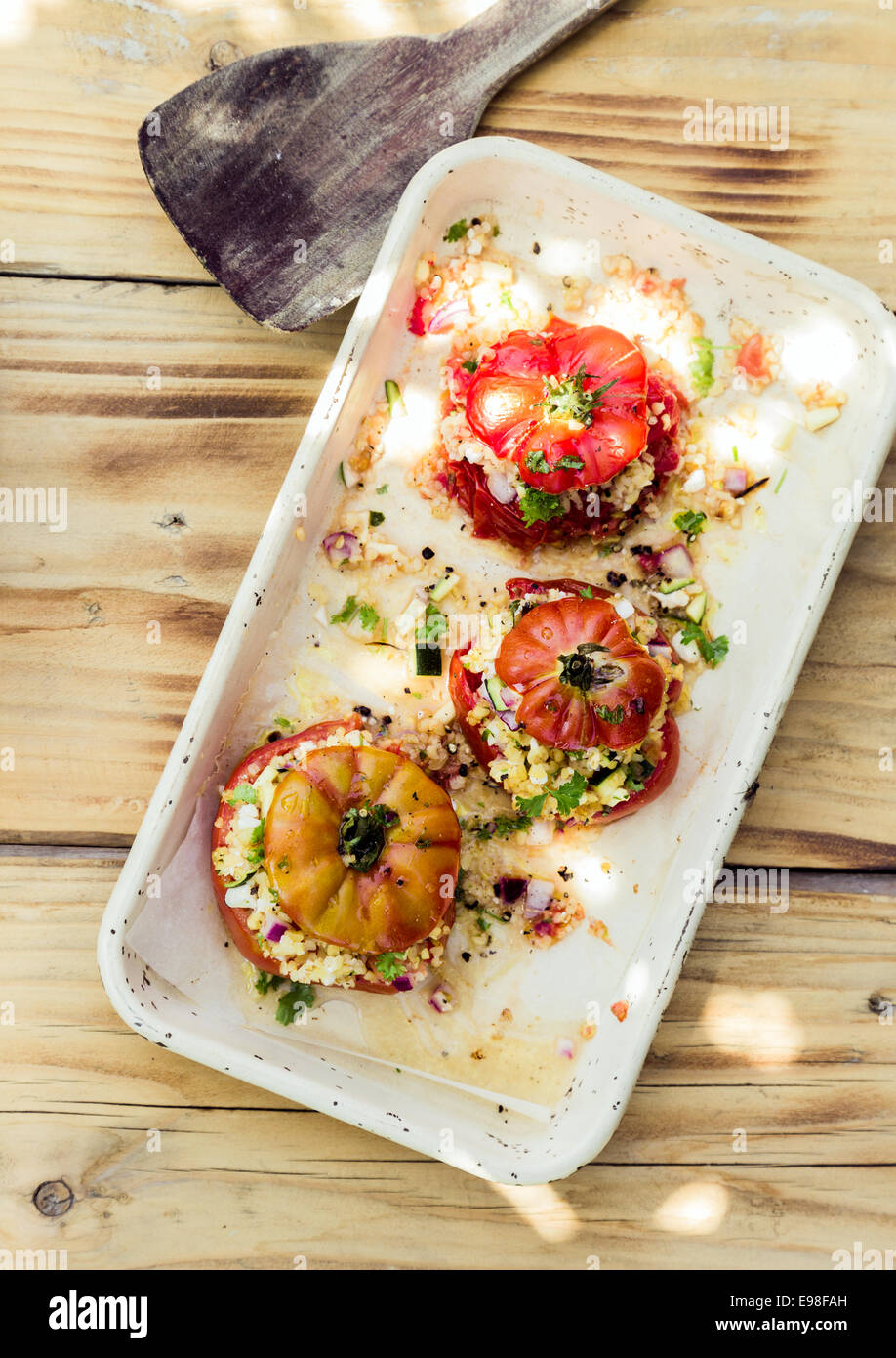 Overhead view of a plate of three ripe red baked tomatoes stuffed to overflowing with herbal grains for a healthy nutritious vegetarian meal Stock Photo