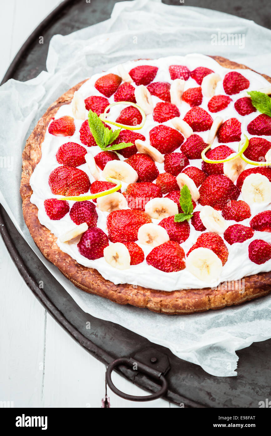 Healthy fresh strawberry and banana tart or pie with cream on a freshly baked golden pie crust served on a baking tray and oven Stock Photo