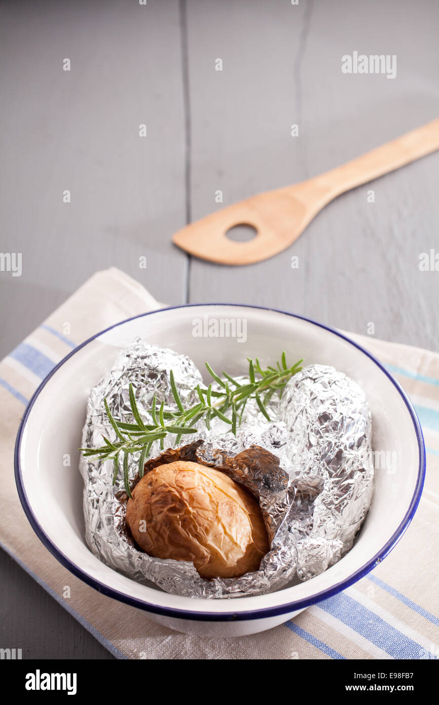 Baked jacket potato in aluminium foil hot off the barbecue lying on the