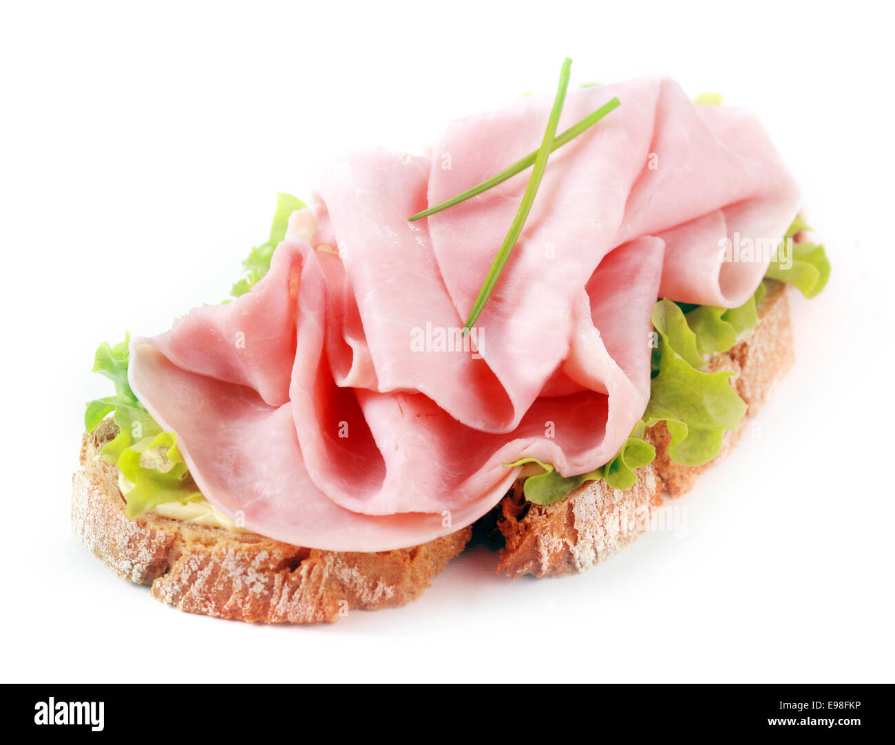 Open ham sandwich on a crusty slice of rye bread with fresh chives and lettuce over a white background Stock Photo
