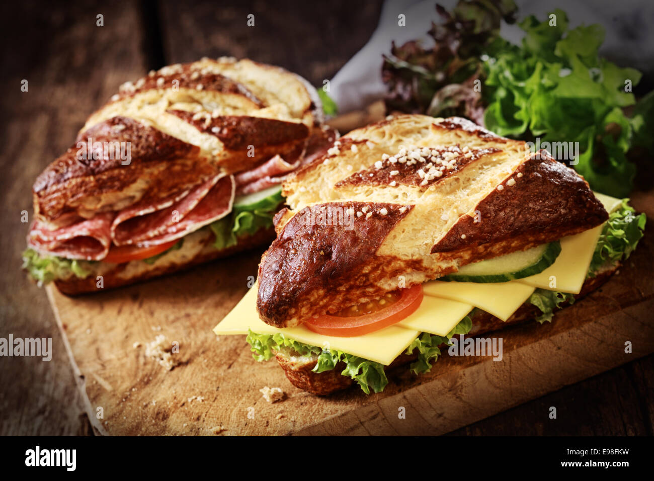 Lye bread rolls , a German and Bavarian speciality bread glazed and baked with lye, with cheese and salami with fresh lettuce, tomato and cucumber on an old wooden board Stock Photo
