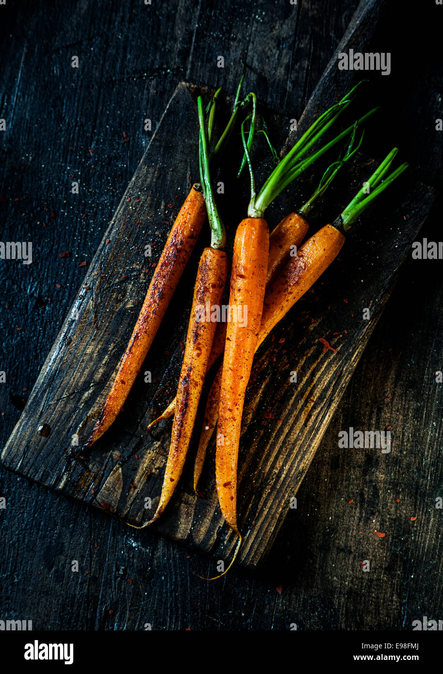 Pile of fried fresh young whole carrots ready to be eaten served on an old grungy rustic wooden board, overhead view Stock Photo