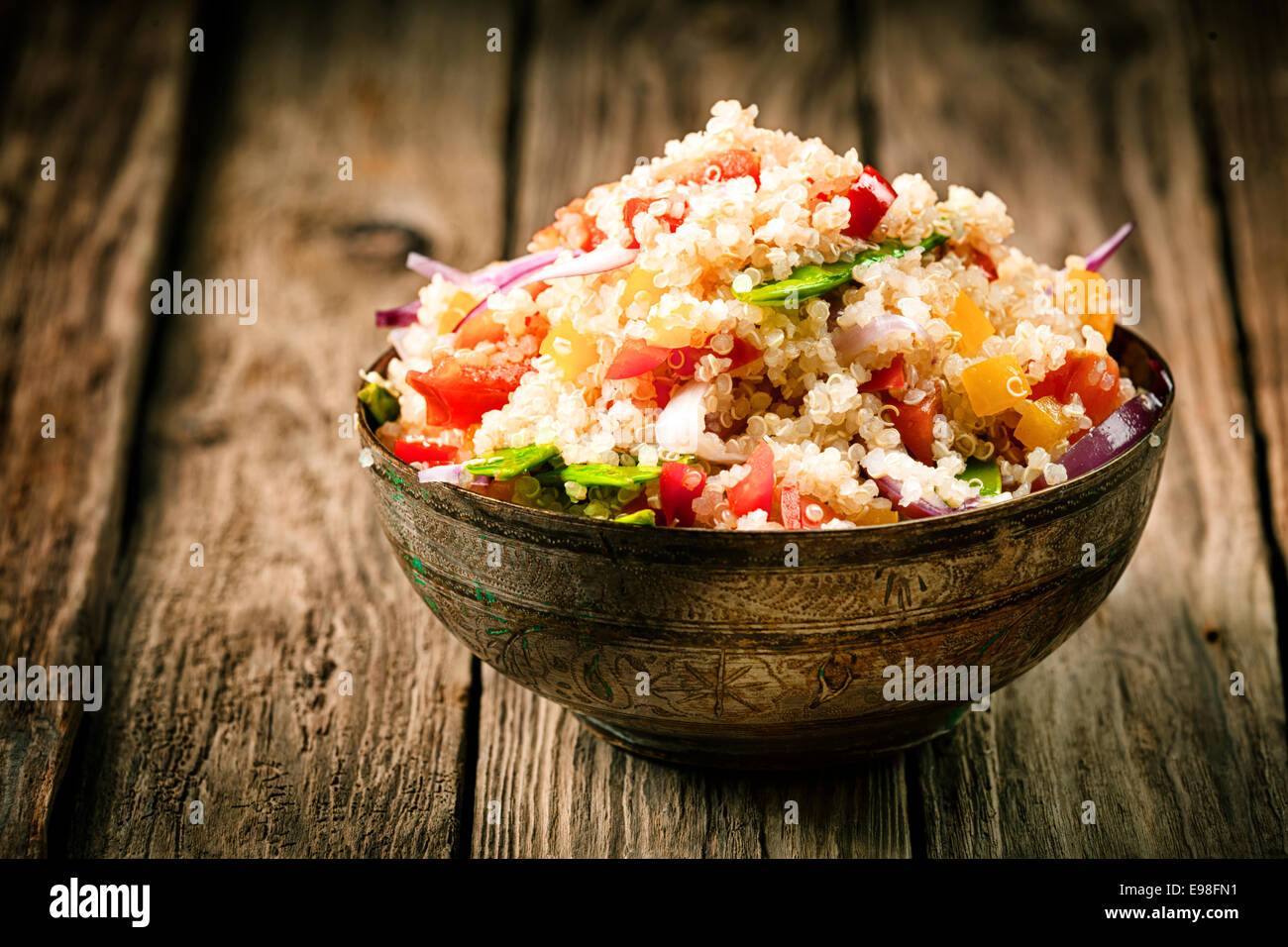 Heaped rustic bowl of savory quinoa with herbs, peppers and tomato for a healthy vegetarian dish rich in protein and nutrients standing on old wooden boards Stock Photo
