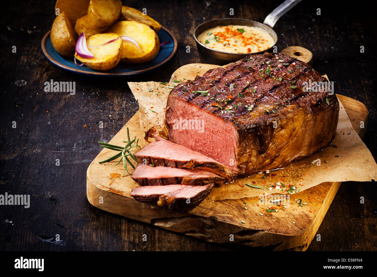 Delicious lean rare roast beef seasoned with fresh herbs and rosemary and carved ready to serve with golden roast potatoes Stock Photo