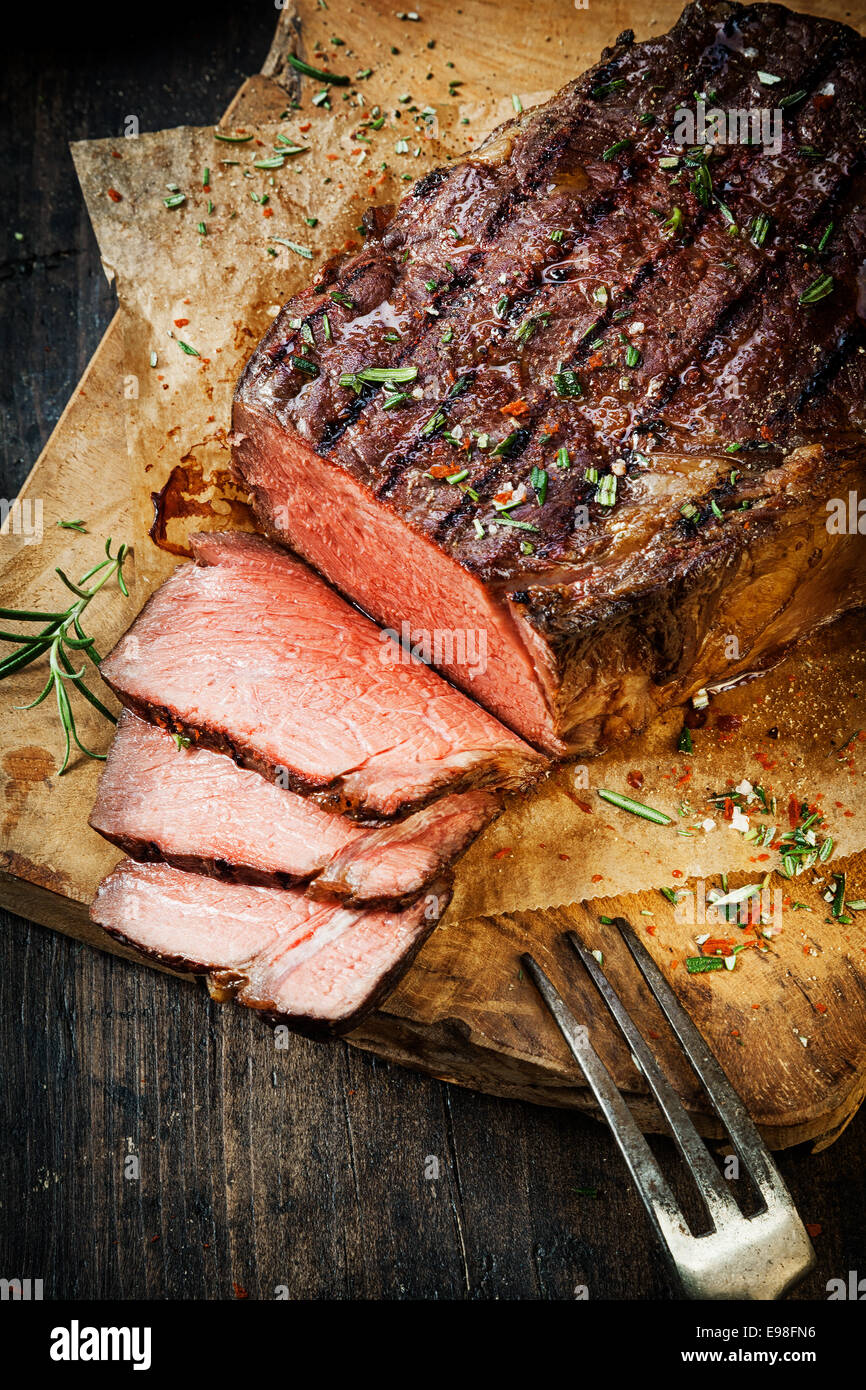 Delicious tender rare roast beef seasoned with fresh herbs and spices being carved on a wooden