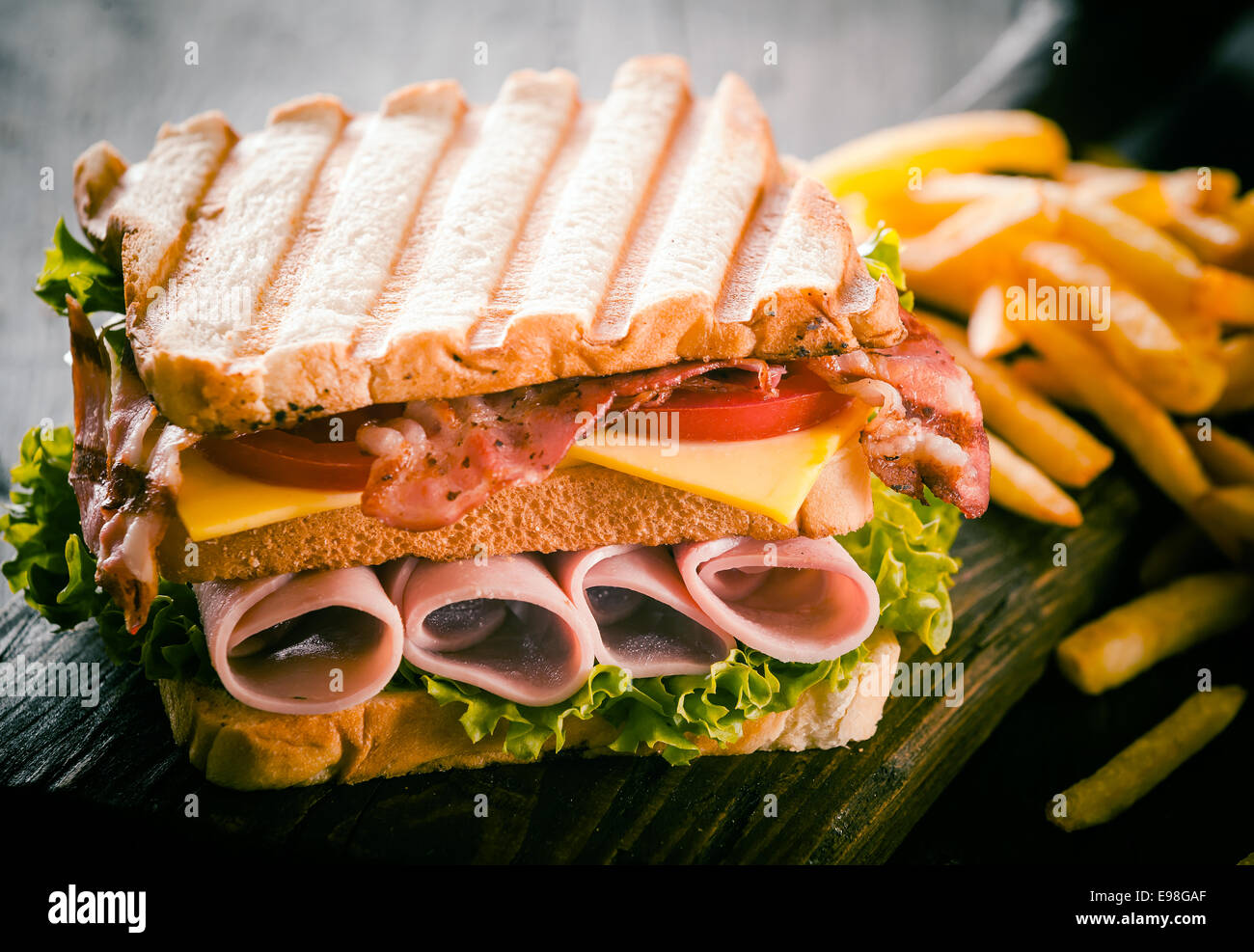 Toasted or grilled ham and cheese club sandwich with fresh lettuce and tomato and a side serving of potato chips, close up view Stock Photo