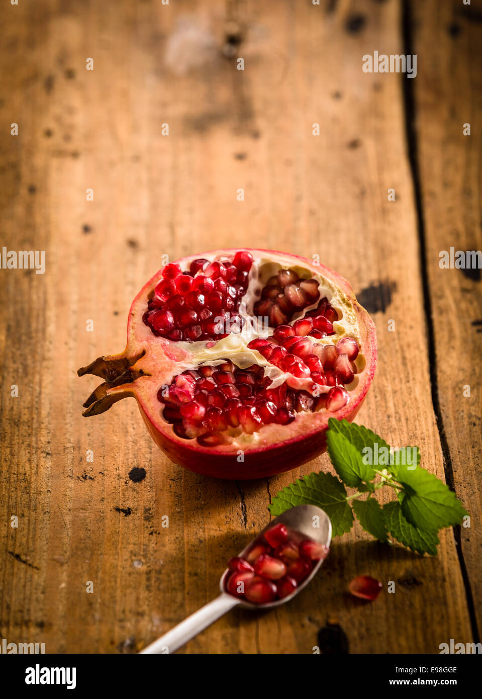 Halved fresh pomegranate with seeds in a teaspoon rich in vitamins and used in ayurvedic medicine on a rustic wooden table with Stock Photo