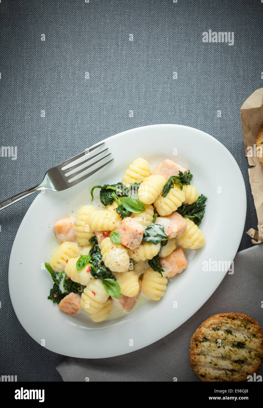 Traditional Italian cuisine with a plate of gnocchi pasta, or dumplings, made with semolina and served with basil and grilled salmon cubes, view from above on grey with copyspace Stock Photo