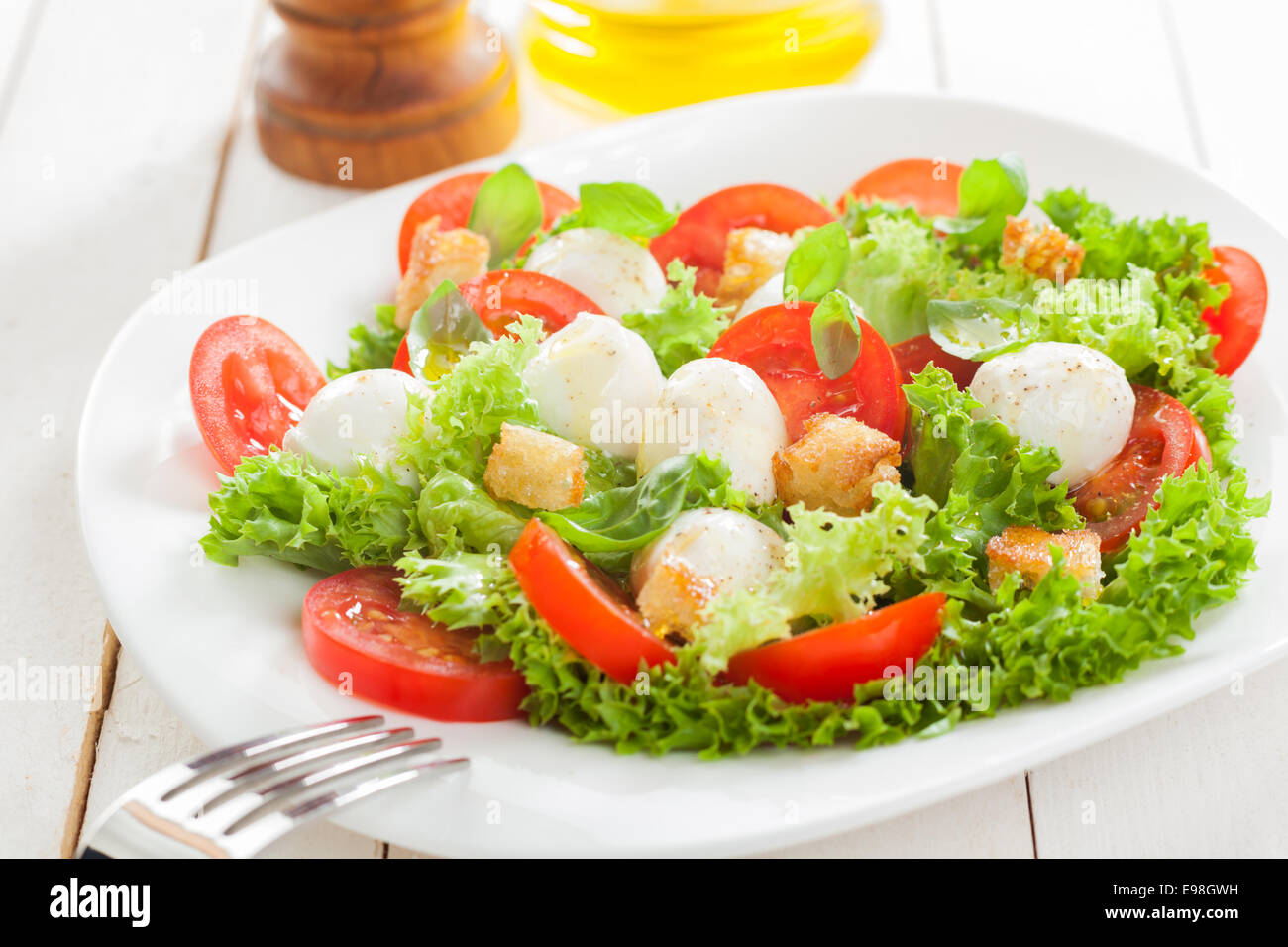Delicious Italian mozzarella salad with crunchy fried bread croutons, sliced fresh tomato herbs and frilly lettuce served on a plate on white wooden boards Stock Photo