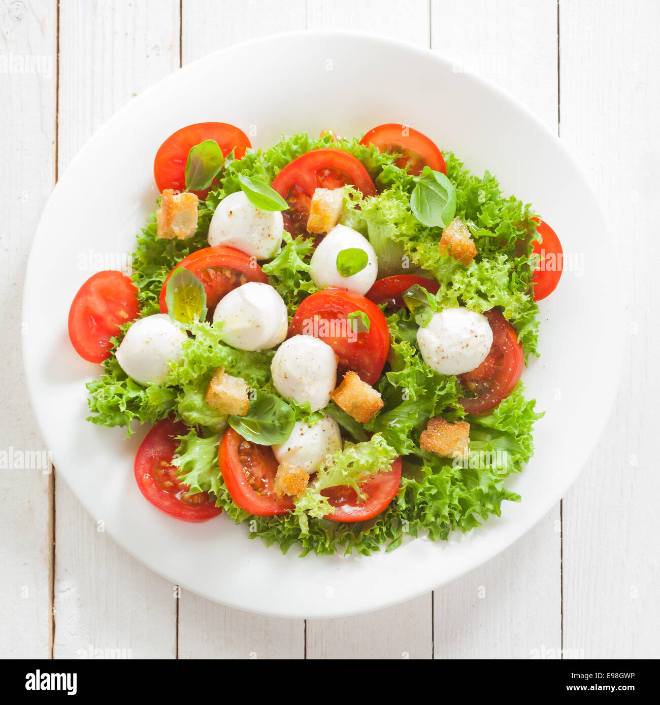 Italian mozzarella cheese and tomato salad with tomatoes and crisp crunchy fried bread cretins, view from above on a plate on white wooden boards, square format Stock Photo