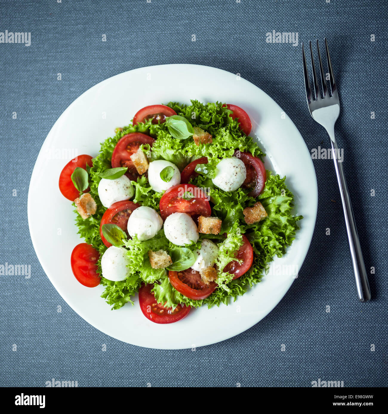 Mozzarella salad with crunchy fried croutons, tomato and frilly lettuce garnished with fresh basil leaves, overhead view Stock Photo