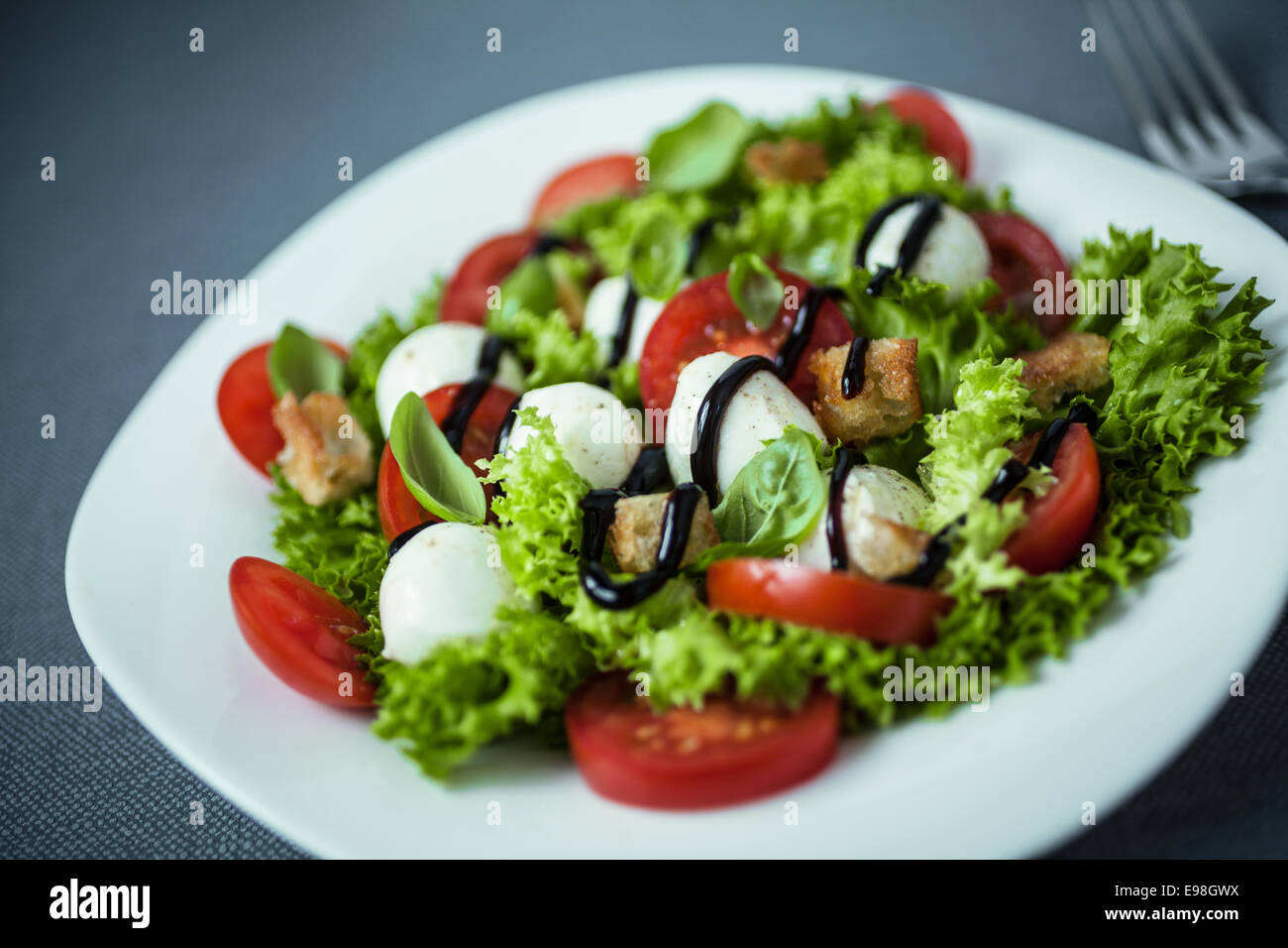 Italian salad with mozzarella pearls, tomato, crunchy croutons and lettuce drizzled with sauce or dressing, close up high angle Stock Photo