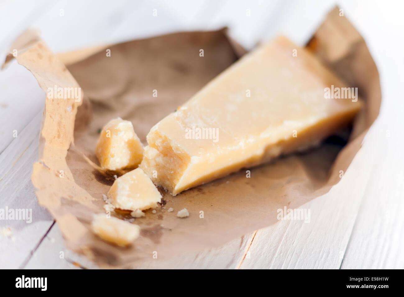 Wedge of fresh matured Italian Parmesan cheese or Parmigiano-Reggiano in a torn brown paper wrapper on white boards for use in Mediterranean cuisine Stock Photo