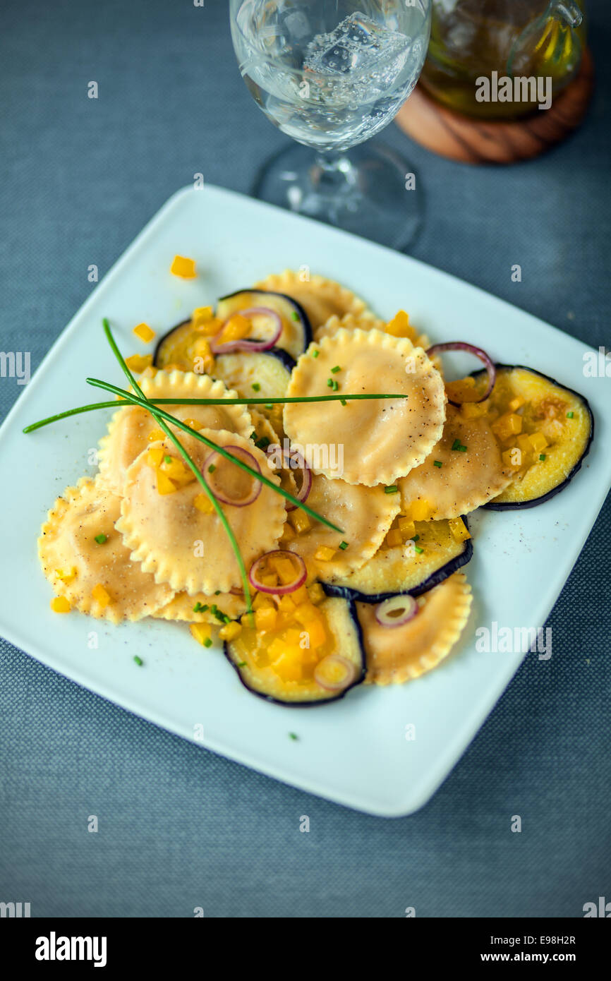 Delicious Italian vegetarian cuisine with round girasole ravioli and aubergine or eggplant topped with chives and served with a Stock Photo