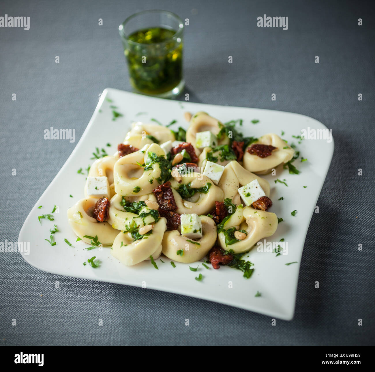Italian tortellini pasta with feta cheese and basil and pine nut pesto drizzled with virgin olive oil on a modern stylish plate Stock Photo