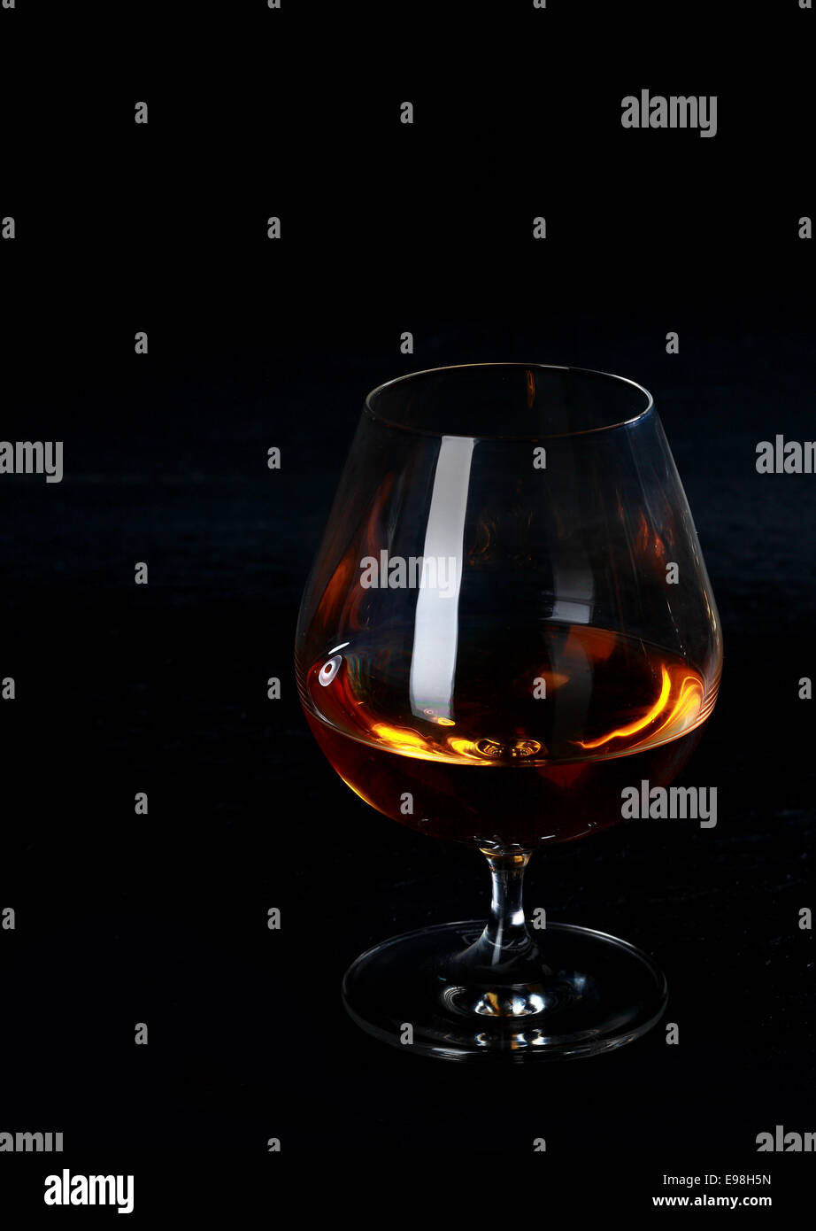 Glowing cognac or brandy in a snifter standing on a dark bar counter in a in the