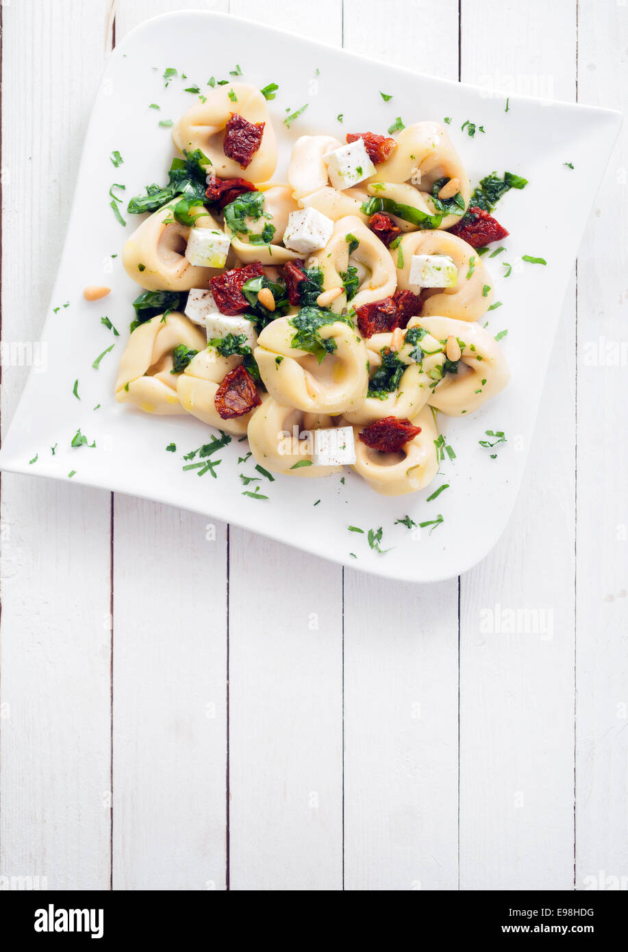 Tortellini pasta with fresh herbs, a spicy piquant sauce and feta cheese on an elegant plate on a white wooden table with copyspace Stock Photo