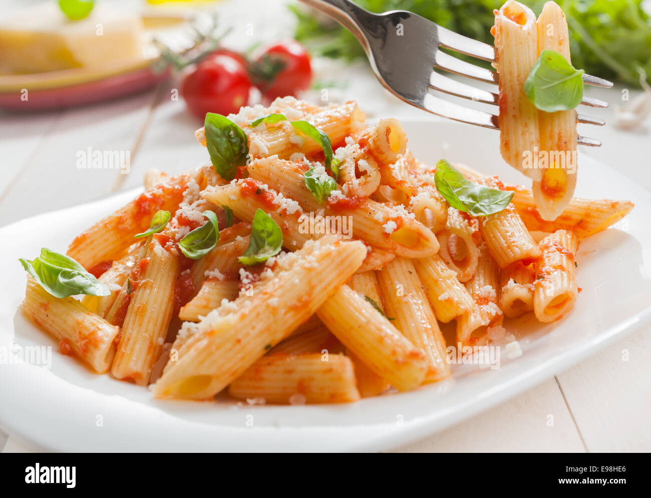 Delicious savory Italian penne rigate pasta with fresh basil and grated parmesan cheese served with a salad with a fork with two pasta tubes suspended above the plate Stock Photo