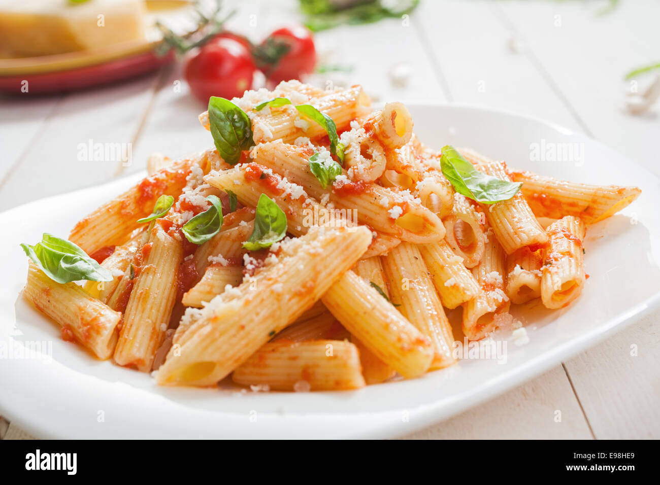 Serving of spicy savory italian penne pasta garnished with fresh basil and topped with grated Parmigiano-Reggiano, or parmesan, Stock Photo