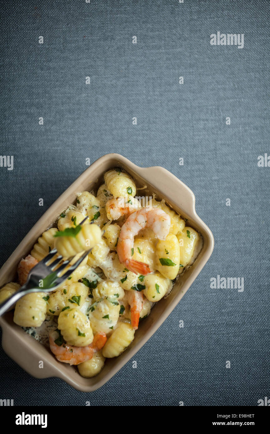 Overhead view of a dish of Italian gnocchi pasta, or semolina dumplings, with shrimps and fresh herbs with one pasta raised on a fork on grey with copyspace Stock Photo