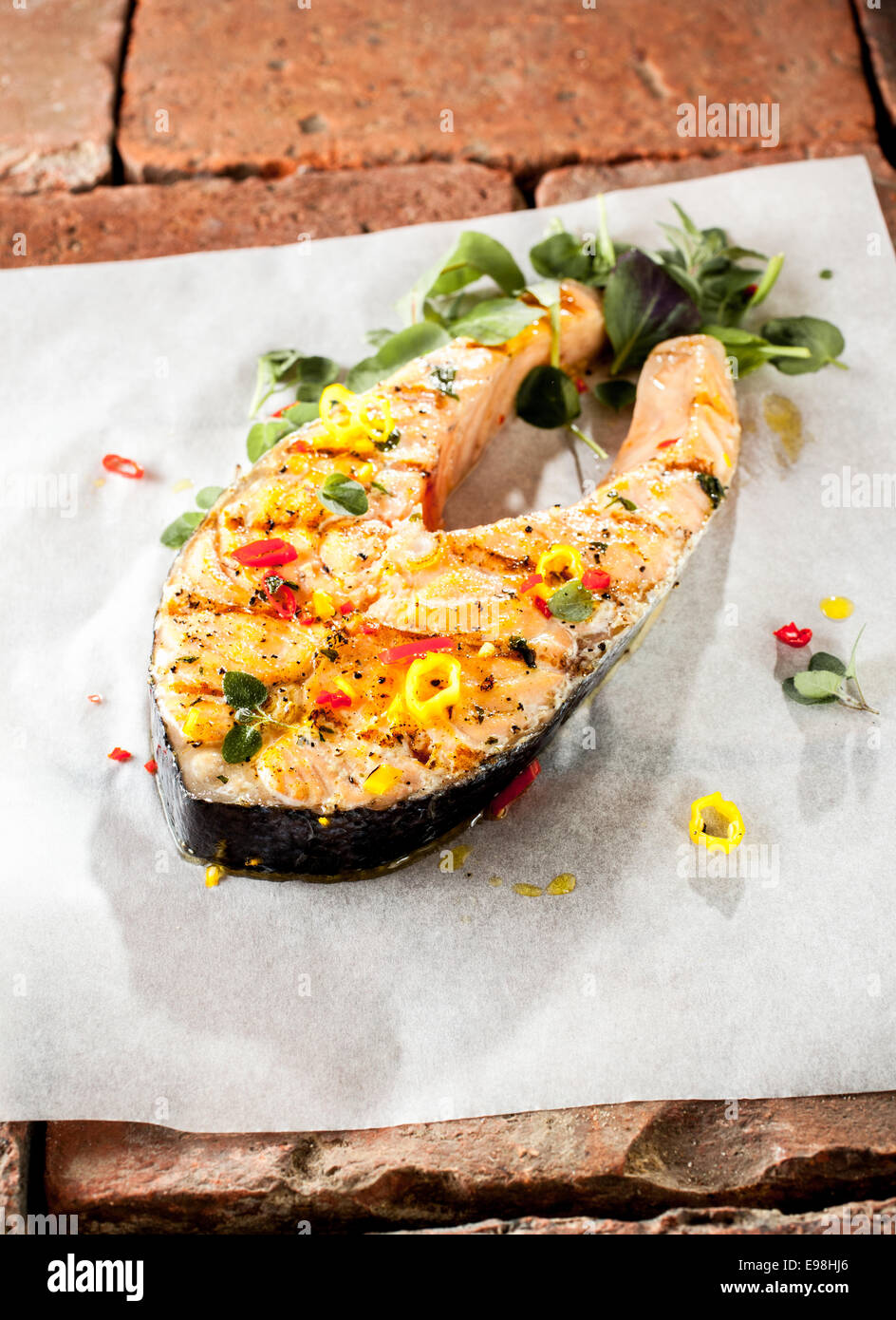 Grilled salmon cutlet with fresh herbs and spices for a tasty savory seafood meal served on a white paper on a layer of bricks Stock Photo