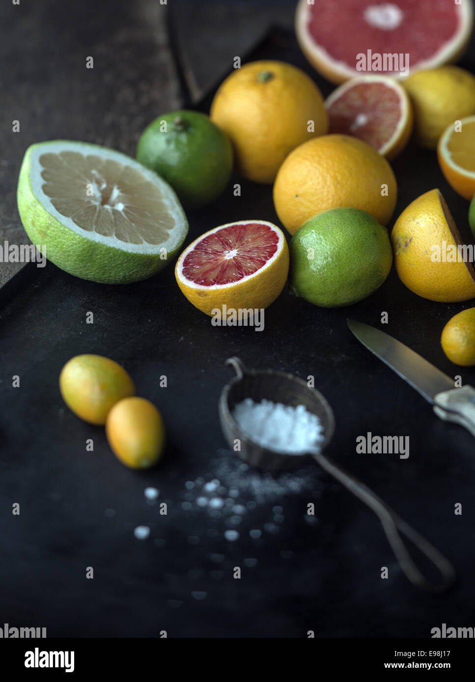 Preparing assorted citrus fruit for dessert with whole and halved grapefruit, oranges, limes, lemon and kumquat on a rustic kitchen counter with powdered sugar and a knife Stock Photo