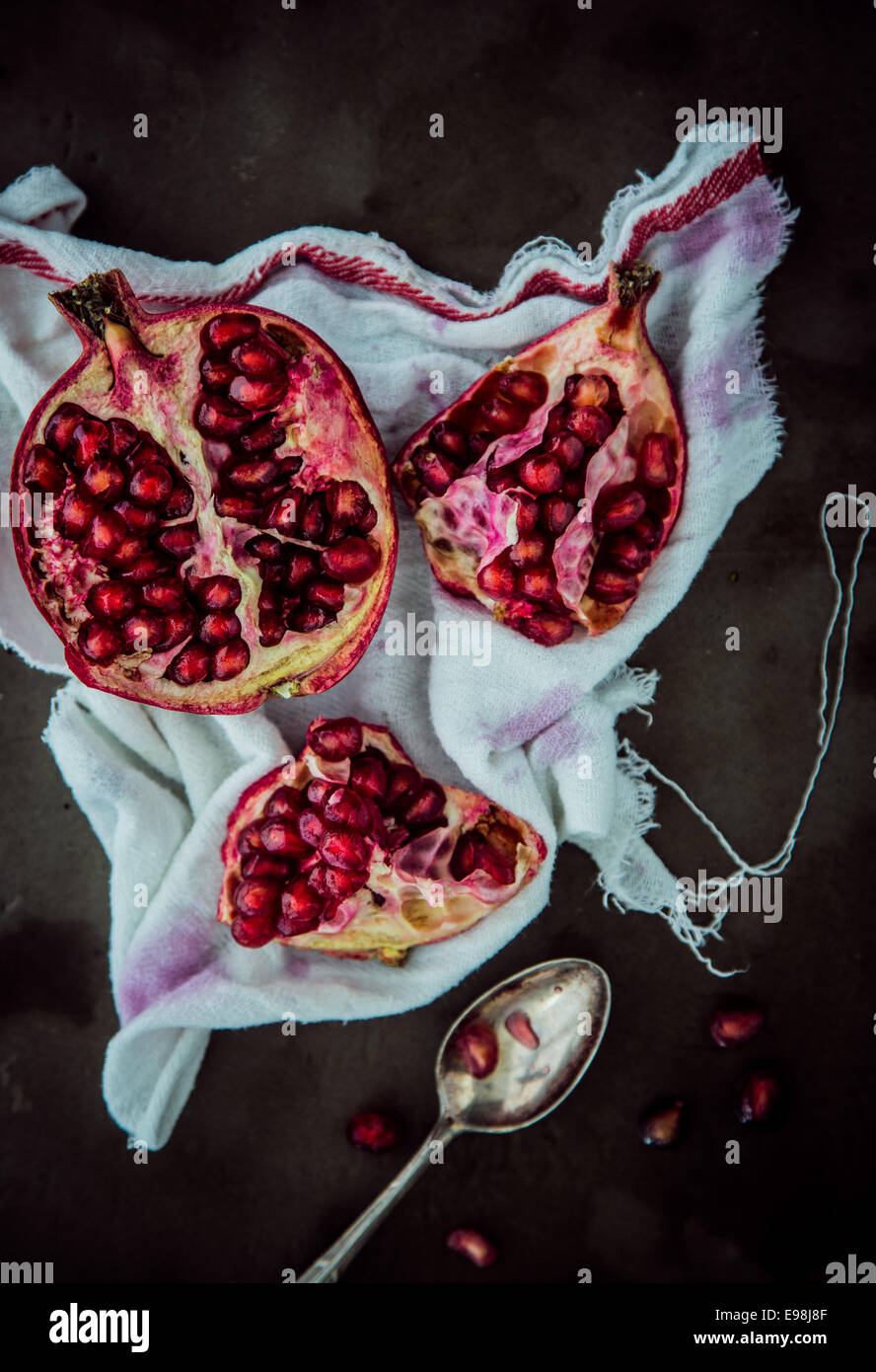 Broken open fresh pomegranate displaying the juicy ripe red seeds on a cloth stained by juice, overhead view Stock Photo