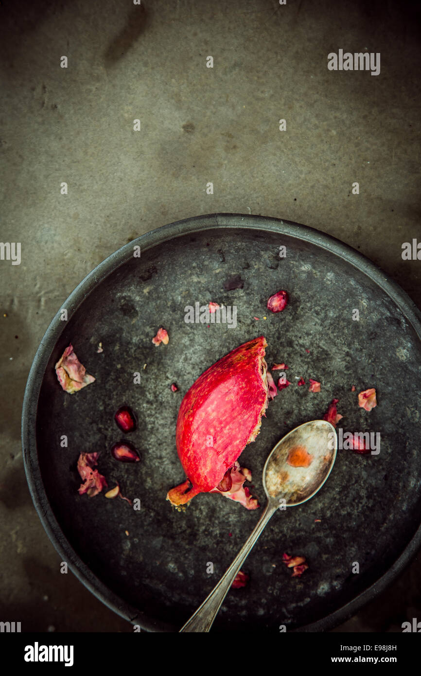Partial remnants of a fresh pomegranate on a rustic plate with a spoon used to remove and eat the juicy ripe red seeds, overhead view with copyspace Stock Photo