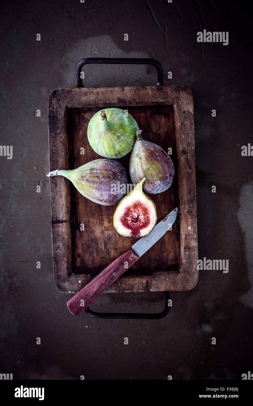 View from above of whole and halved ripe juicy fresh figs in an old vintage container in a rustic kitchen with a knife and copyspace Stock Photo