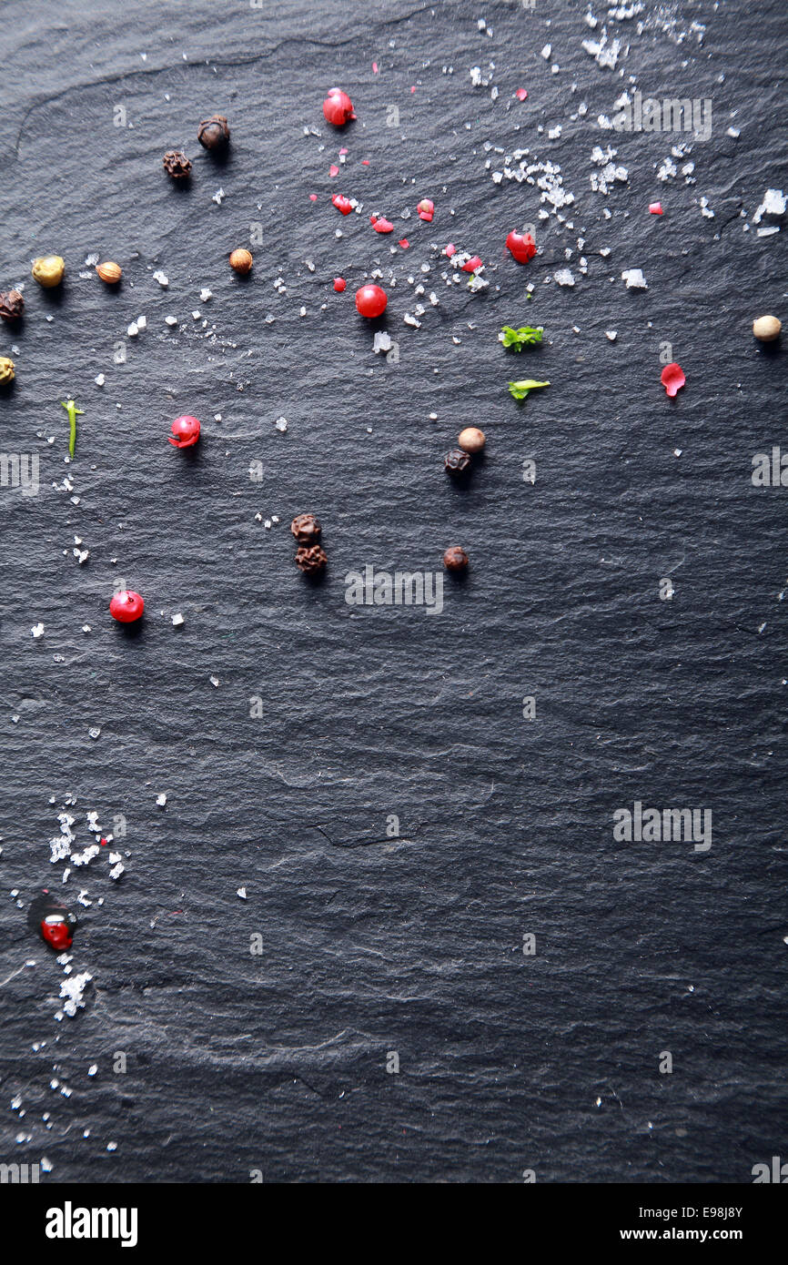 Assorted whole peppercorns and salt scattered on a background of textured dark natural slate with copyspace Stock Photo