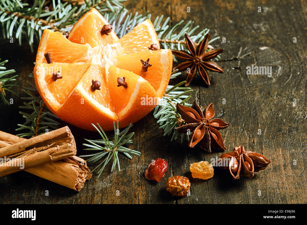 Decorative spicy orange Christmas still life with a cut fresh orange nestling in a pine branch with stick cinnamon, star abise and nuts on a rustic wooden background with copyspace for your greeting Stock Photo