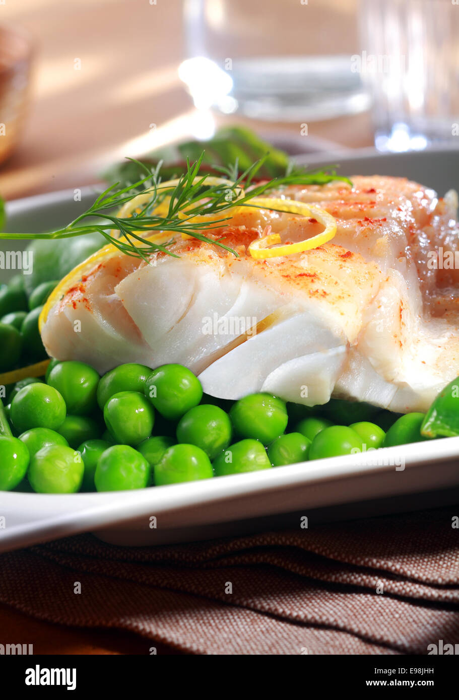 Delicious seafood meal of grilled or oven-baked fish fillet served with juicy green petit pois peas , lemon zest and dill at a restaurant Stock Photo