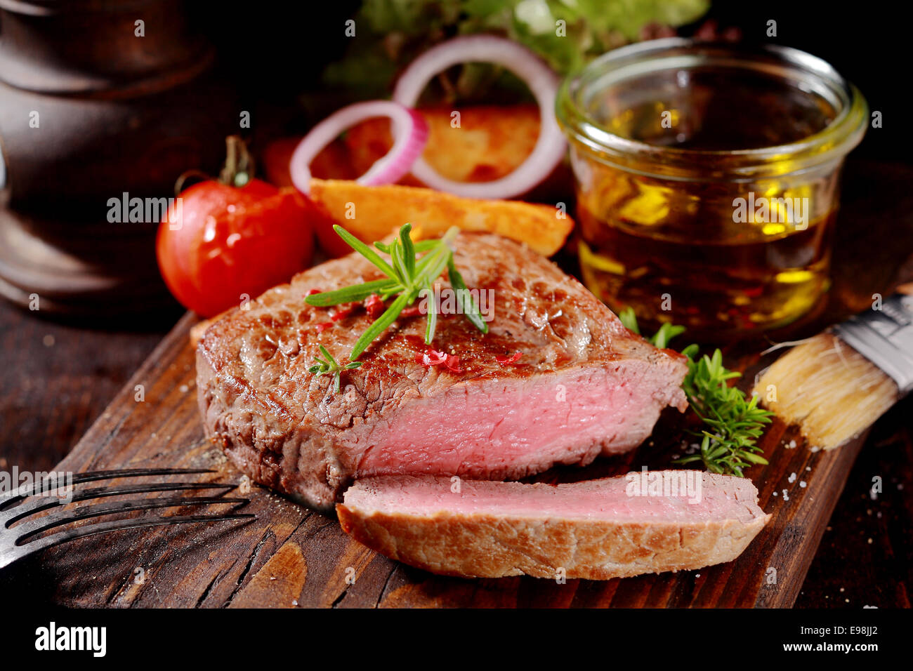 Tender lean medallion of rare grilled beef steak seasoned with fresh herbs cut through to show the texture and served with fresh vegetables on a rustic wooden chopping board Stock Photo