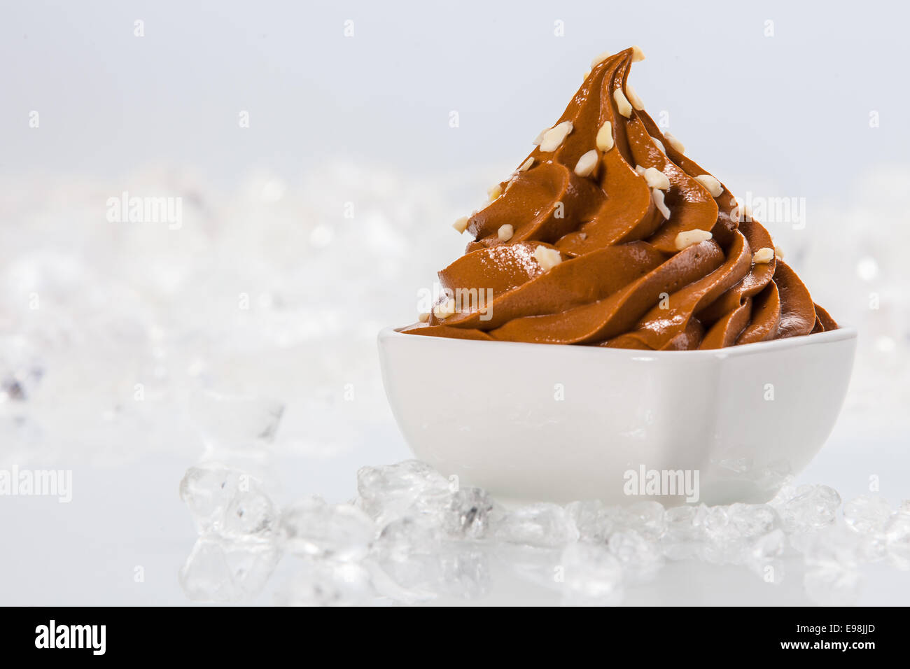 Tasty Brown Frozen Yogurt on White Bowl Surrounded by Ice on Table. Isolated on White Background. Stock Photo