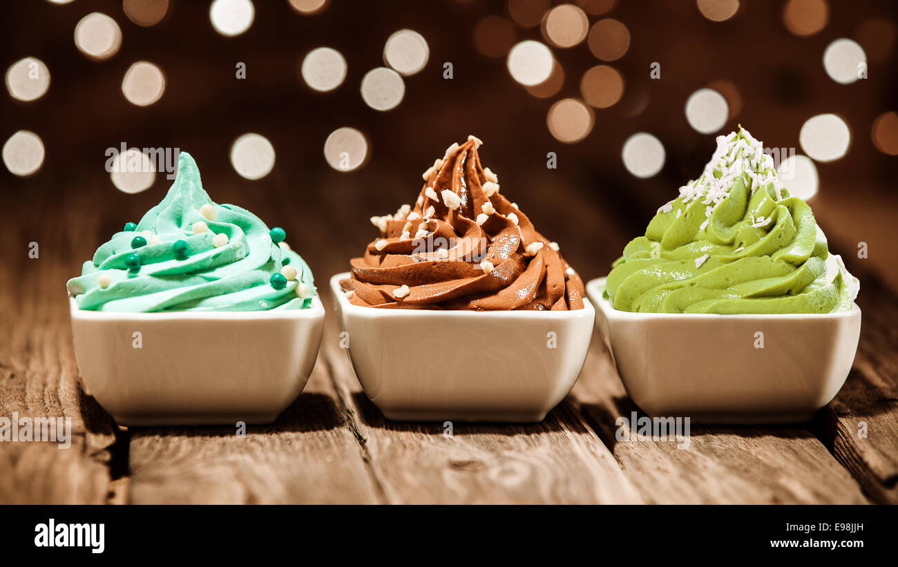 Colorful row of three different frozen yogurt desserts in blue, brown and green garnished with nuts and sugar pearls at a party Stock Photo