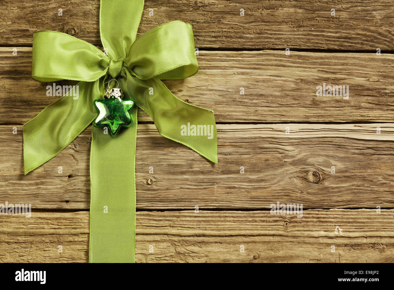 Stylish green ribbon and heart decoration tied in an ornamental bow on textured rustic wooden boards for your Xmas greeting or seasonal message Stock Photo
