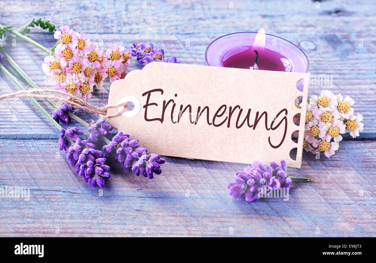 Beautiful delicate blue and lilac colored background depicting - Erinnerung - Memories - with fresh scented lavender spikes, dainty flowers and a burning aromatic candle on blue rustic wooden boards Stock Photo