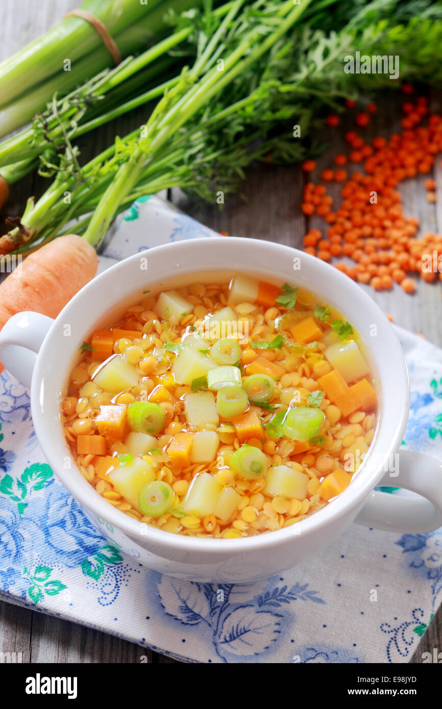 Delicious nutritious country cuisine with a bowl of carrot, leek and lentil vegetable soup, high angle view with bunches of fresh leeks and carrots and dried lentils Stock Photo
