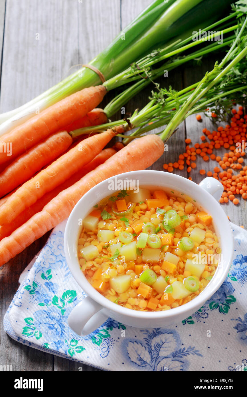 Nutritious lentil, carrot and leek soup served in a bowl surrounded by fresh bunches of carrots, leeks and dried orange lentils Stock Photo