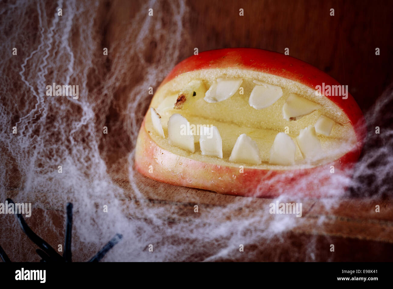 Ghoulish gaping Halloween mouth with teeth made from an apple on a wooden shelf festooned with spider webs in a scary festive background for Allhallows Eve Stock Photo