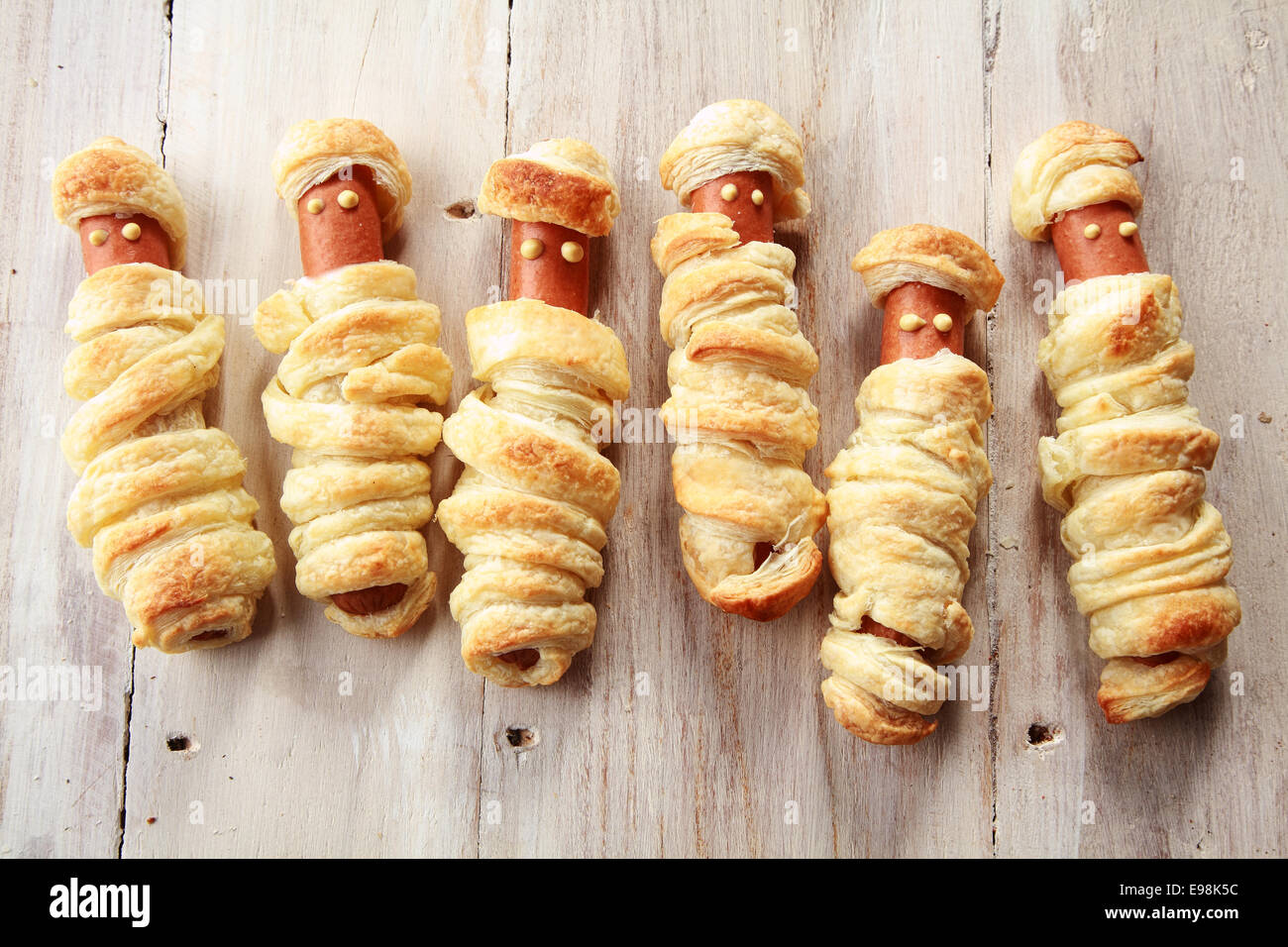 Six Weiners Wrapped in Pastry to Look Like Halloween Mummies on Wooden Background Stock Photo