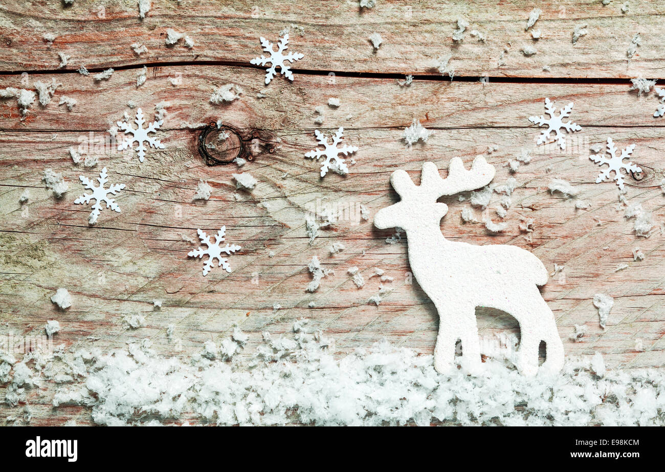 Christmas background with a reindeer in snow with falling decorative snowflakes on an old rustic wooden board Stock Photo