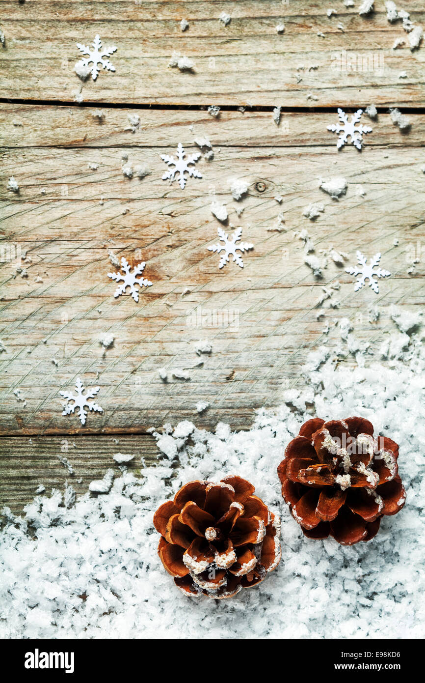 Christmas or Advent pine cone background with snow and failing snowflake decorations on a weathered rustic wood background with Stock Photo